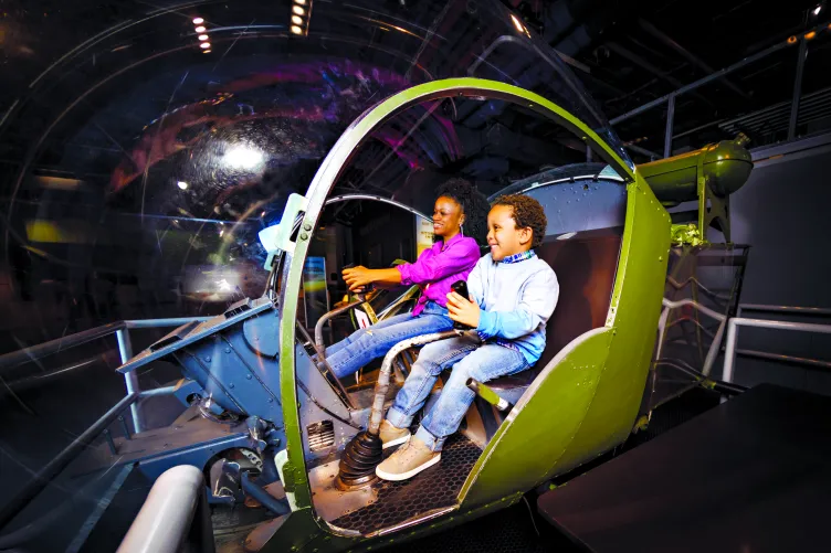 mage of children climbing into and sitting in a mock cockpit of an Intruder aircraft in the Museum's Exploreum.