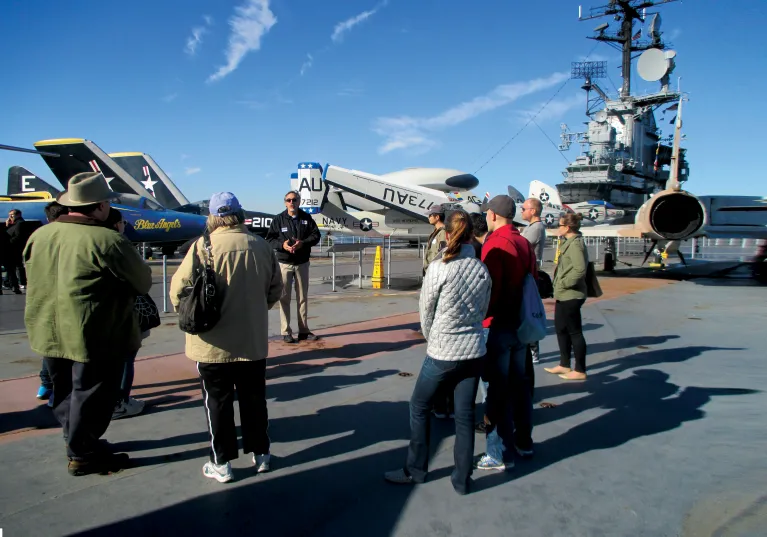 Group of visitors with a museum educator at the flight deck with various aircraft in the background.
