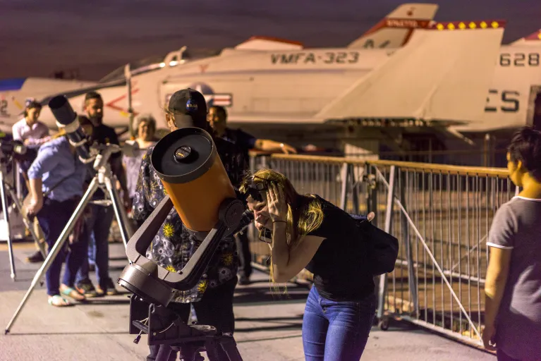 Woman looking through a telescope at an Astronomy Night Event at the Intrepid's Flight Deck.