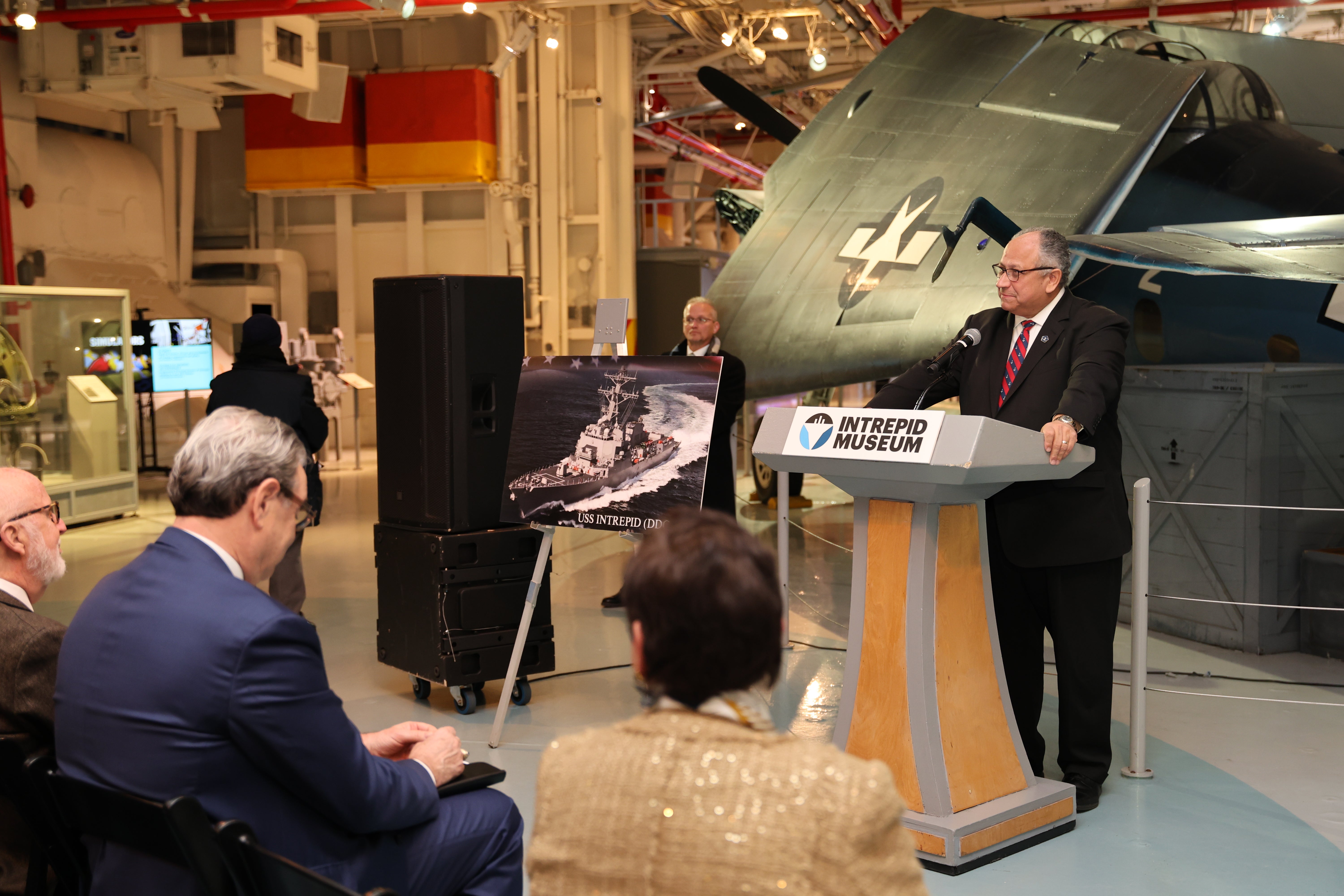 Secretary of the Navy Carlos Del Toro at a podium at the Intrepid Museum.