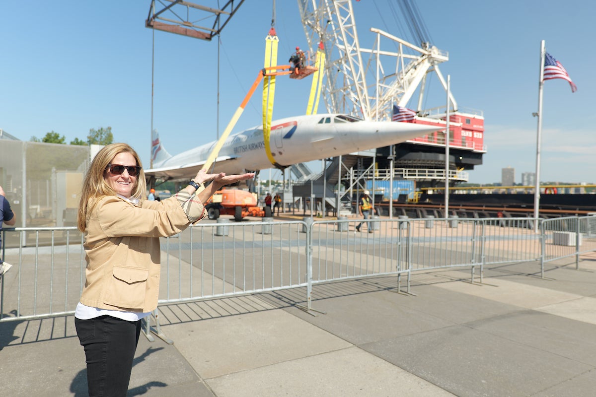 
President Susan Marenoff-Zausner posing in front of Concorde during the plane's arrival to the Museum. Credit: The Intrepid Museum. 