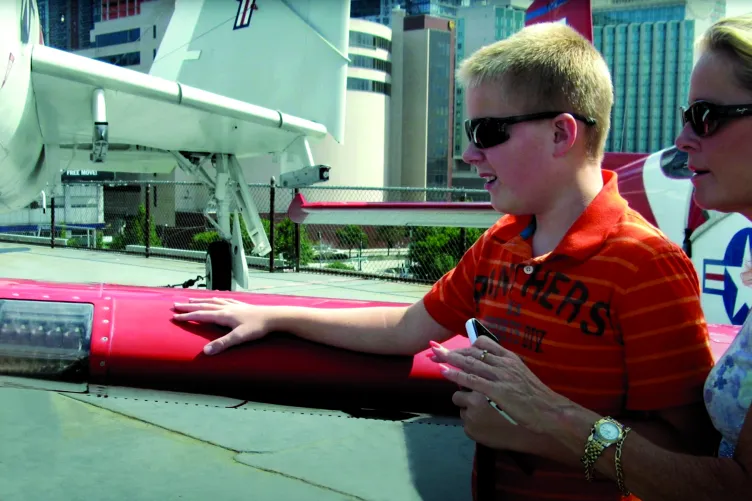 A mother looks on as her young son touches the wing of an aircraft.