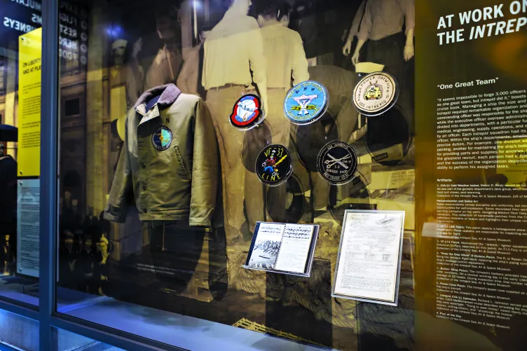 An exhibition case that displays a military jacket and several notable patches.