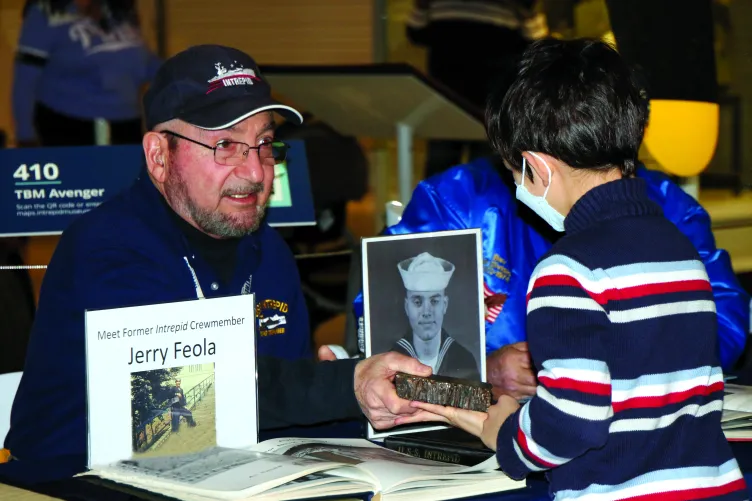 Former Crew Member Jerry Feola is showing a child an artifact at a display table.