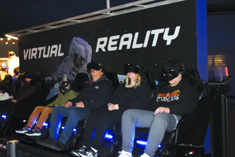Visitors are seated in a row and wearing goggles for the Virtual Reality experience.