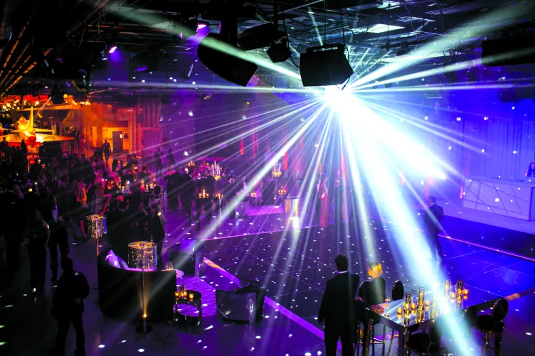 A disco ball lights up a dance floor as people mingle at cocktail tables in the Museum's hangar deck.