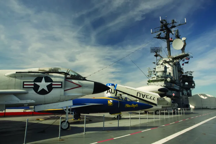 Several airplanes on the flight deck with the island and aircraft restoration hangar in the background.