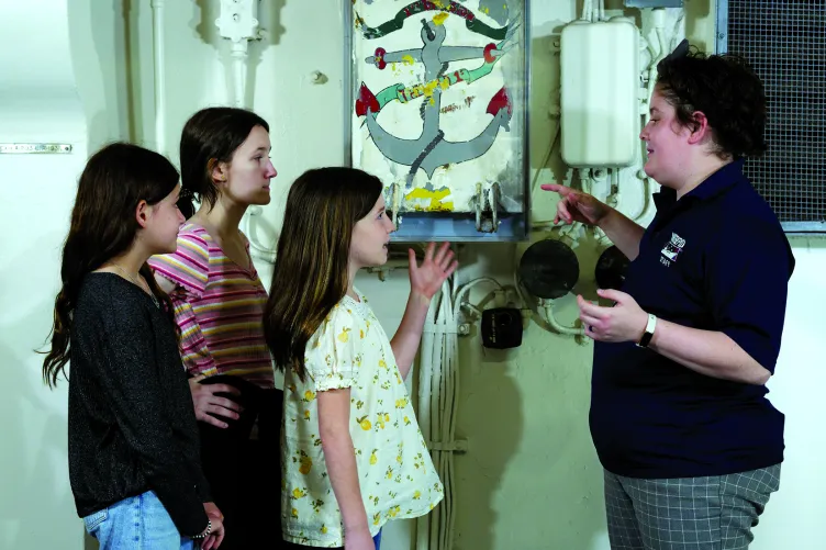 A Museum educator is showing sailor art to a group of kids.