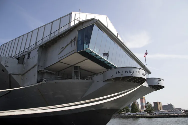 The view of the fantail from the Hudson River where one can see the floor-to-ceiling windows and an American flag flying.