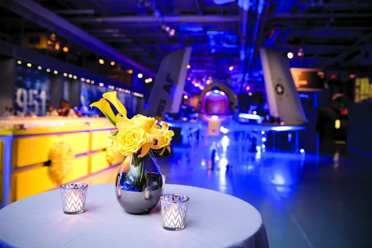 Cocktail tables with a bar in the background on the hangar deck