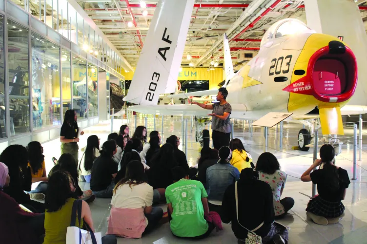 A group of visitors stand with a tour guide in front of the Avenger.