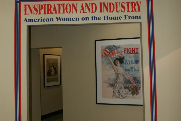 Walls with an opening and text that says “Inspiration and Industry: American Women on the Home Front” and patriotic posters of women are framed behind.