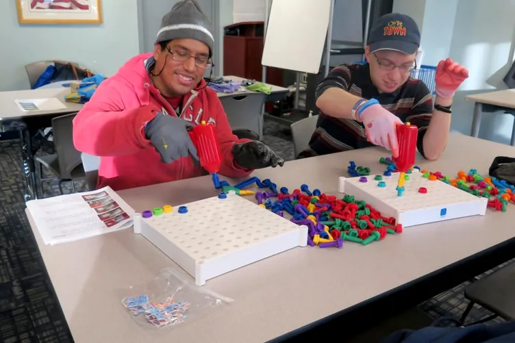 Two students are in a classroom playing with nuts and bolts toys.