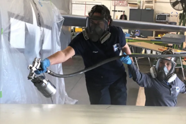 Aircraft restoration technician Rosie Grogan applies a top coat of paint to the wing with the assistance of restoration volunteer Kate Good.