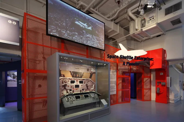 An exhibition that says “Space Shuttle Enterprise: A Pioneer” with a large screen showing the spacecraft being carried by an airplane.