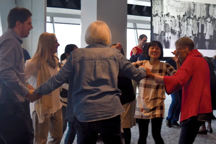 Visitors are standing in a circle and holding hands dancing.
