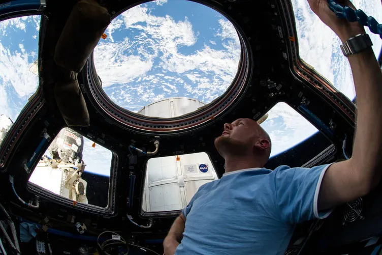 A man in a light blue shirt is in a space capsule and is looking up at a beautiful blue sky.