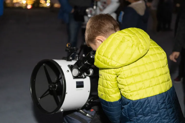 A boy is looking through a telescope.