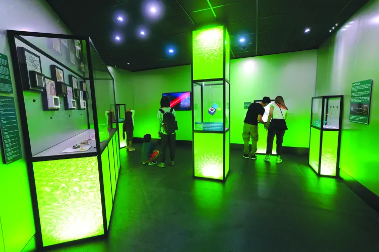 Visitors look at panels in an exhibition that is lit with green lighting.