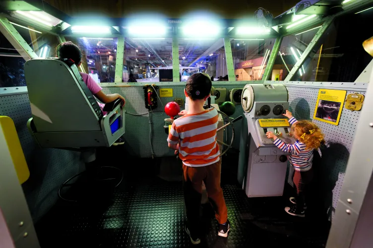 Three children playing with on a replica of a flag bridge on an aircraft carrier.