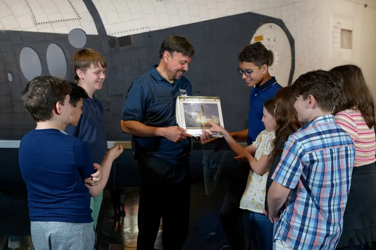 A Museum educator is showing something to a group of students.