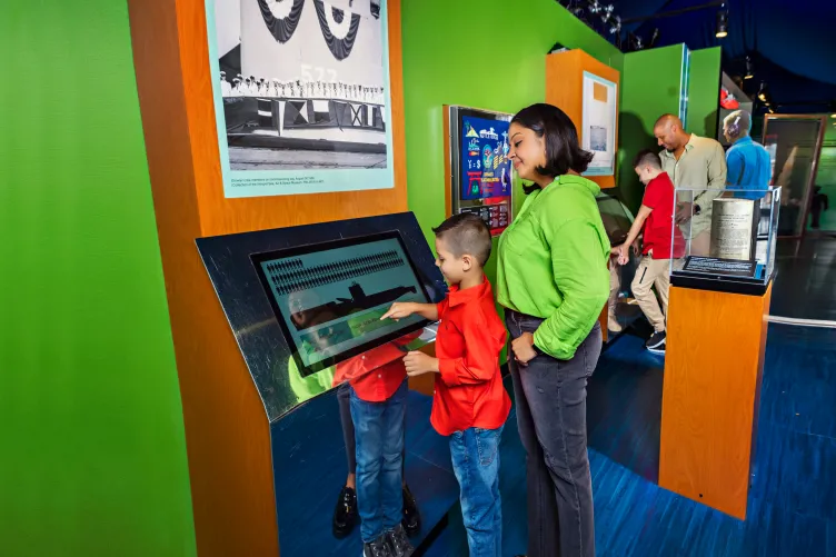 A woman and boy interact with a digital display at the view from the deep: the submarine growler and the Cold War exhibit.