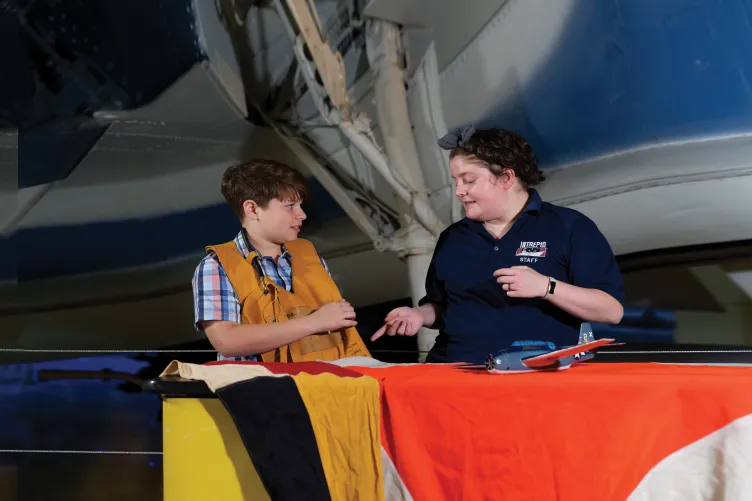 A boy wearing a Pilots floating vest with an Educator at an education station