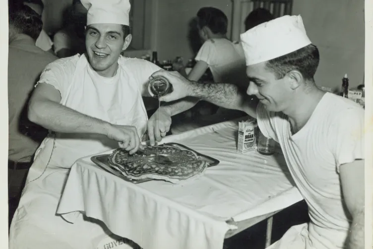 A group of sailors in the mess hall enjoying a huge pancake