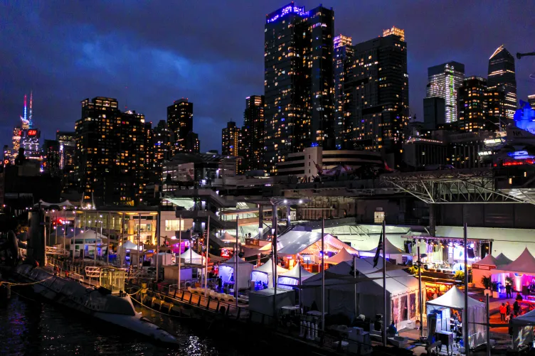 The New York City skyline illuminated at night with glittering skyscrapers and lights reflecting on the water.