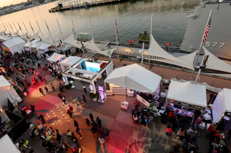 Pier 86 at night, illuminated by vibrant lights with event tents set up, with crowds creating a lively atmosphere.