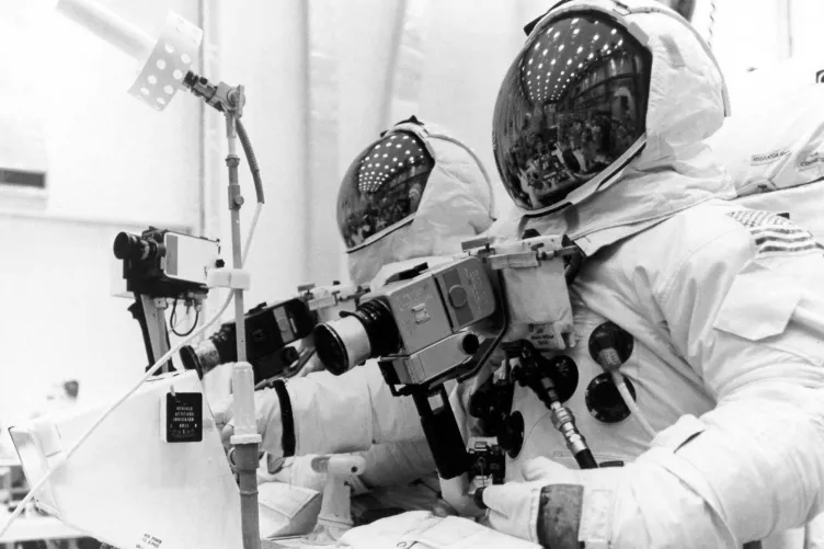 Astronauts in space suits peering through a camera.