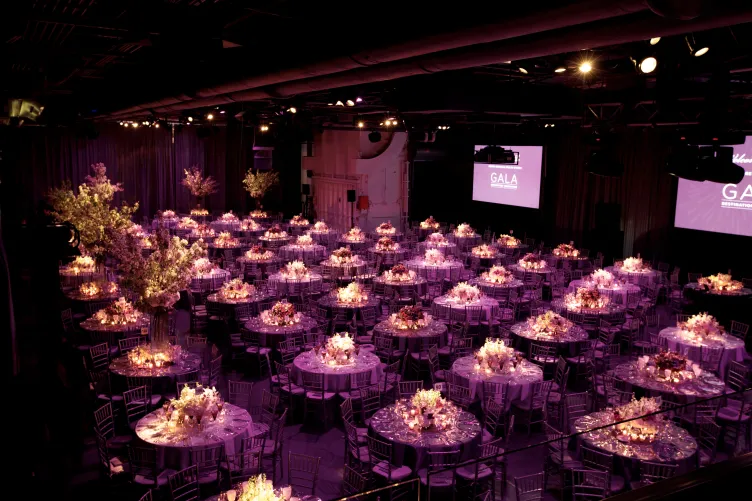 Hangar 3 set for a large seated dinner and program with floral arrangements and pin spot lighting on the tables