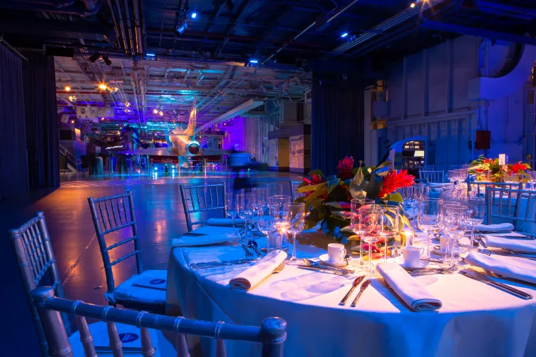 Hangar 2 and Hangar 3 set in blue uplighting, view of Hangar 3 dinner table with florals and overlooking aircraft in Hangar 2