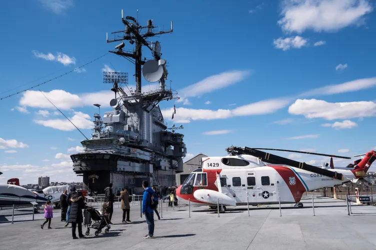 Several airpcraft on the flight deck with the island and aircraft restoration hangar in the background.