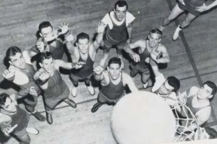 Several men are gathered around a basketball hoop, some with their hands raised. A ball is on the rim.