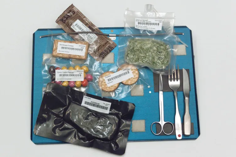 A blue astronaut food tray displaying an assortment of packaged meals and utensils