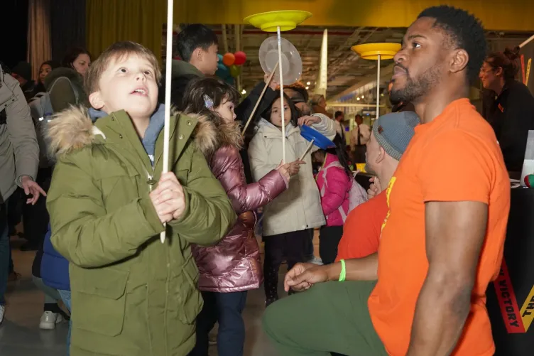 Children learning to spin a plate on their fingers during a Kids Week activity.