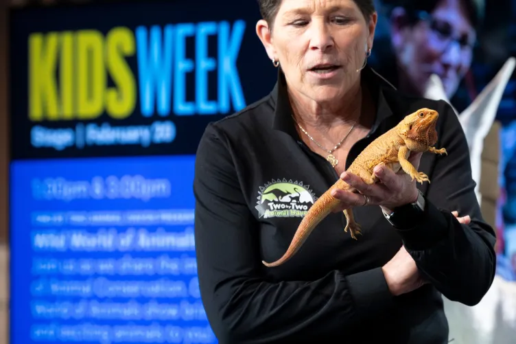 A woman on stage holding an animal during a Kids Week show."