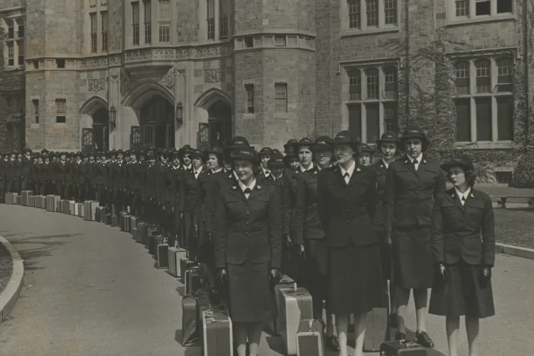  A black-and-white photo of women in uniform lined up in front of a brick building.