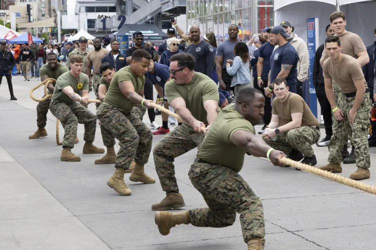 Sailors participating in a lively tug of war competition on Pier 86 during Fleet Week, with a crowd watching.