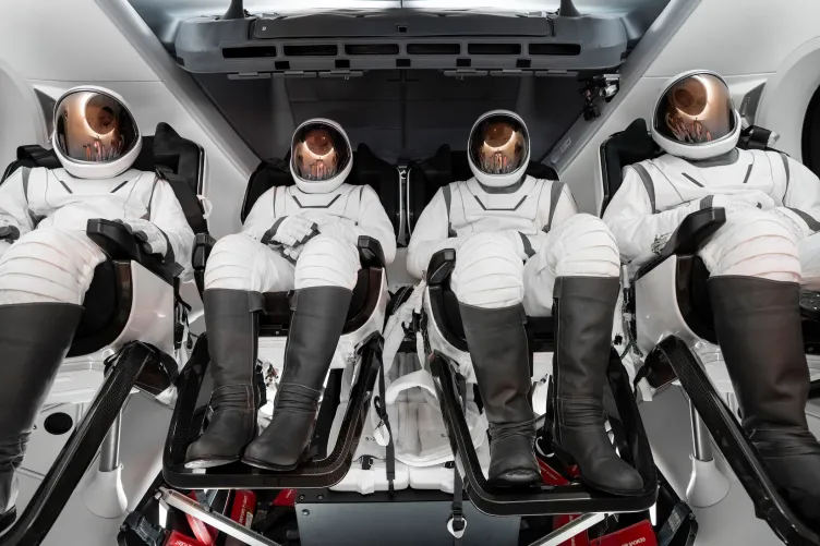 Four astronauts seated in a space shuttle wearing their astronaut suits.