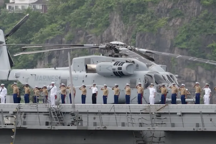 Service members standing in formation and saluting on the deck of an aircraft carrier as it arrives at Pier 86 during Fleet Week.
