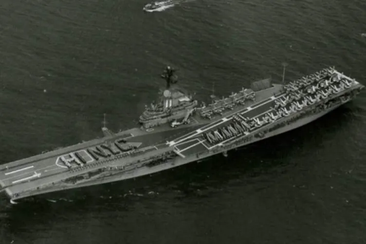 Intrepid at sea with sailors standing on the flight deck in the shape of the words, "HI NYC".