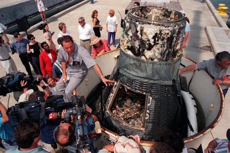 Curt Newport answering questions from the press sitting a top a space capsule.