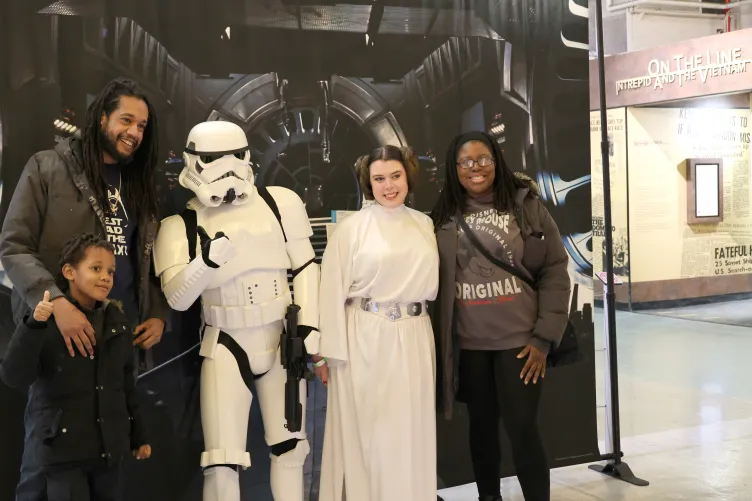 A kid and his parents posing for a picture with a stormtrooper and Princess Leia from Star Wars during Kids Week