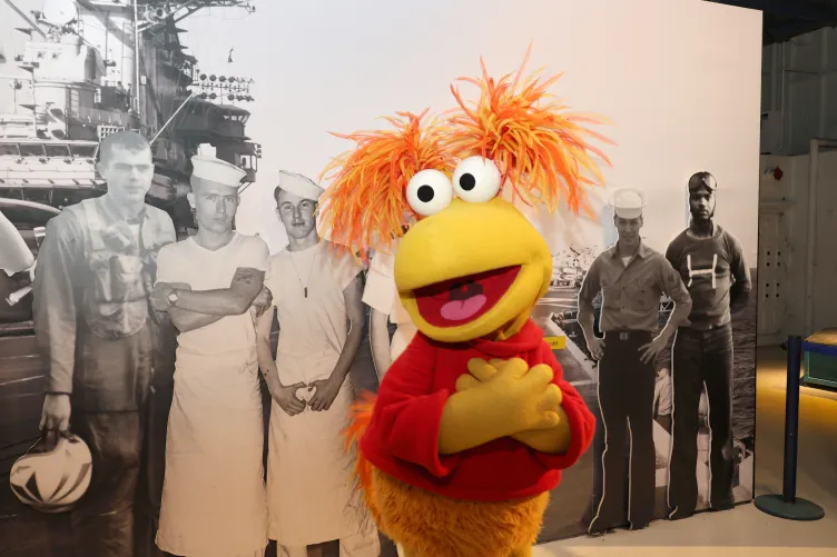 Fragglerock in front of a picture of the Intrepid during it's service