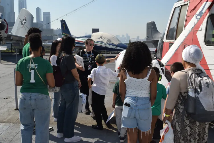 An educator leads a diverse group of children and families in exploring a helicopter on Intrepid's flight deck