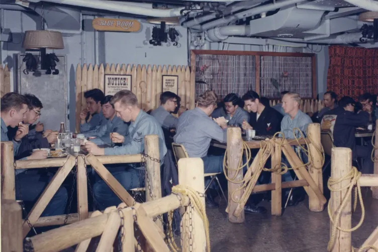 Military personnel seated on the General Mess Deck enjoying a meal and drinks
