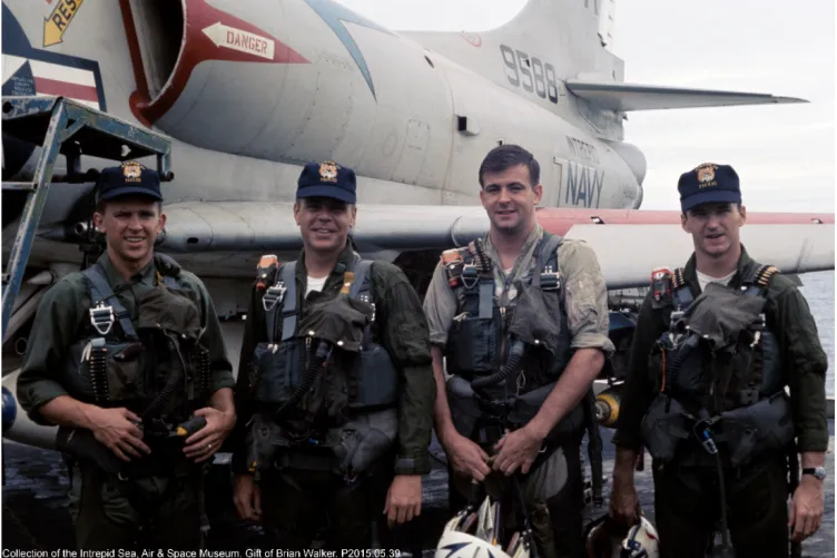 Military crew members standing on the flight deck beside aircraft.