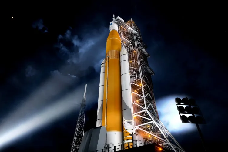 NASA’s Space Launch System rocket illuminated on the launchpad at night, with its orange core stage and white boosters beside the launch tower.